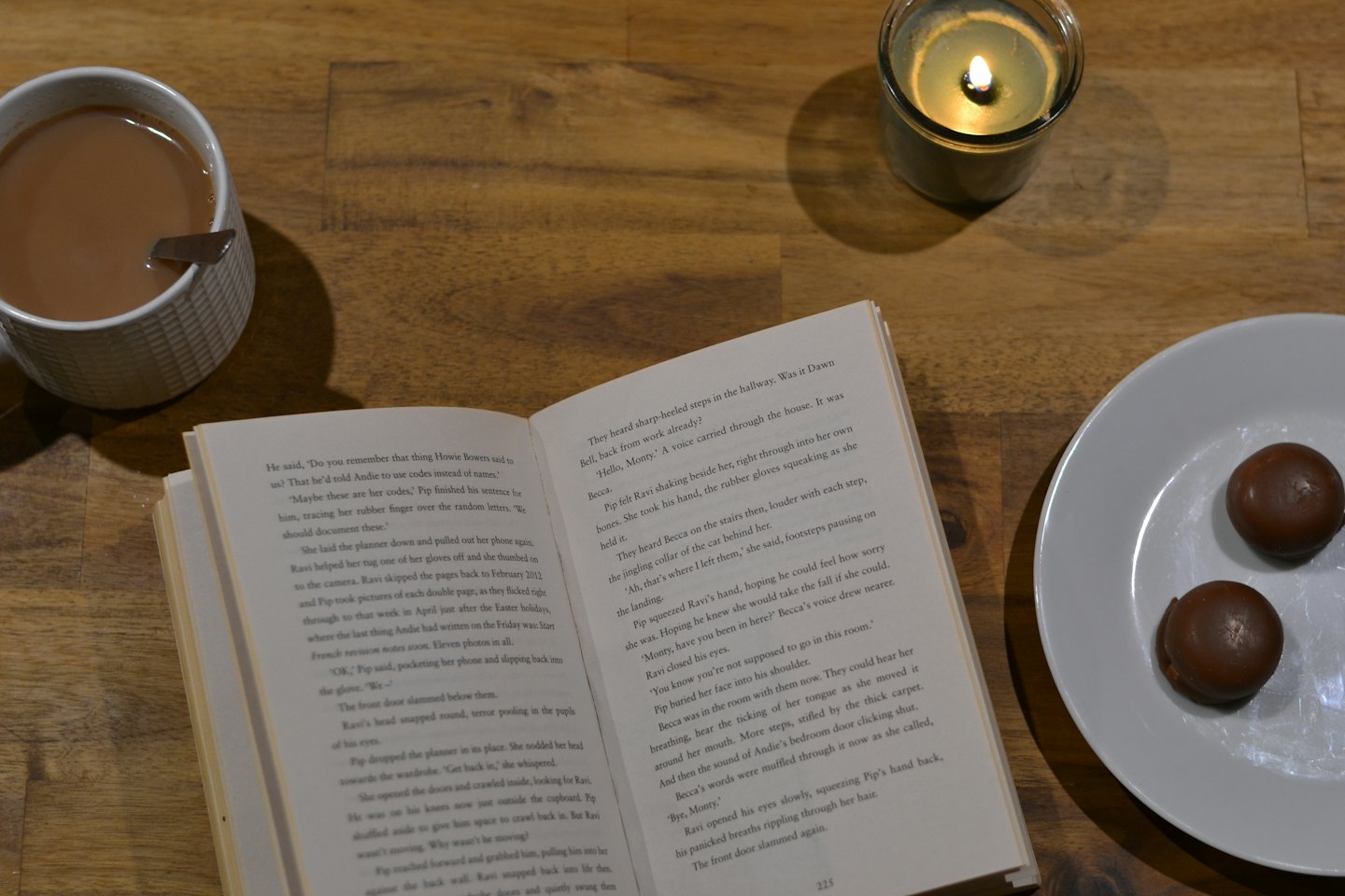 Ein offenes Buch, Tee, Kerze und Schokolade auf einem Tisch.